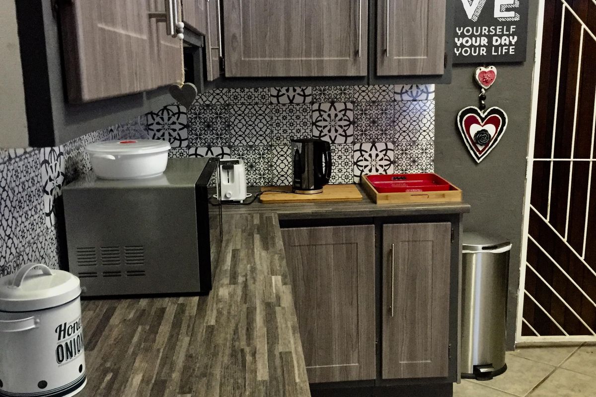 A functional kitchen area featuring wood-look laminate countertops, modern grey cabinetry, and decorative patterned tile backsplash with ceramic floor tiling.