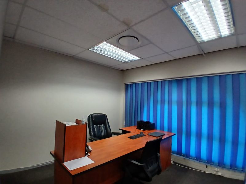 A functional office space featuring a suspended ceiling with integrated lighting, vertical window blinds, and carpeted flooring.