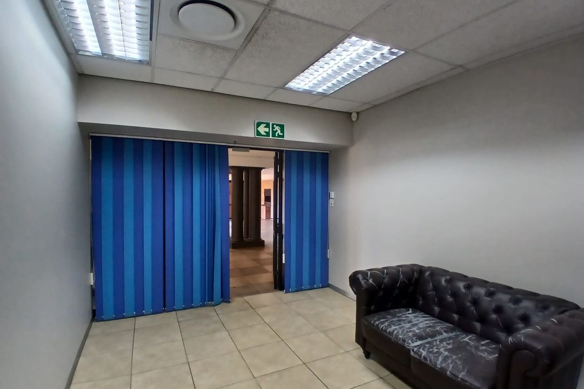 Office space featuring ceramic floor tiles, suspended ceiling with integrated lighting, and vertical blinds leading to an adjacent area.