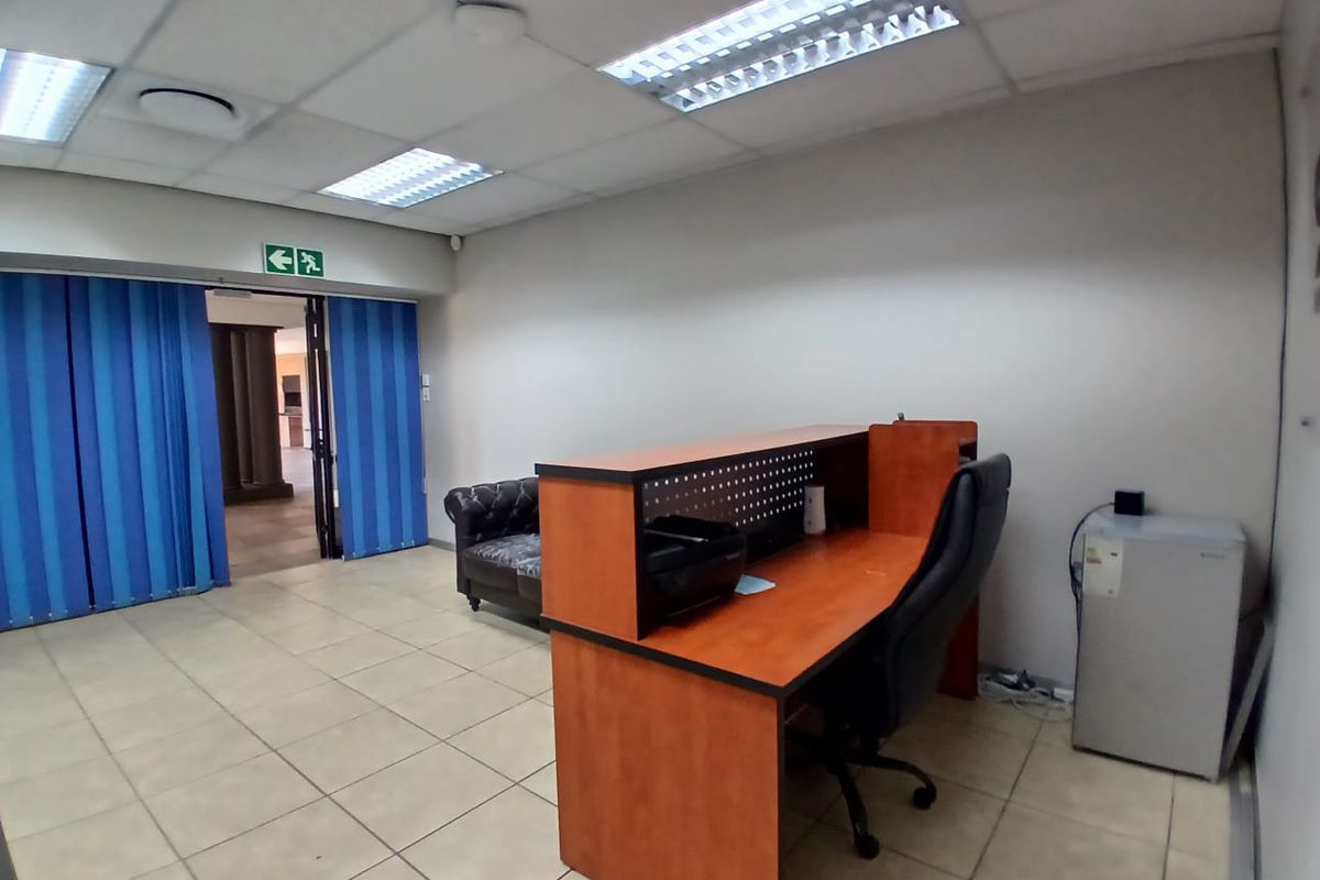 A functional office space featuring a suspended ceiling with recessed lighting, ceramic tiled flooring, and blue vertical blinds covering the doorway.
