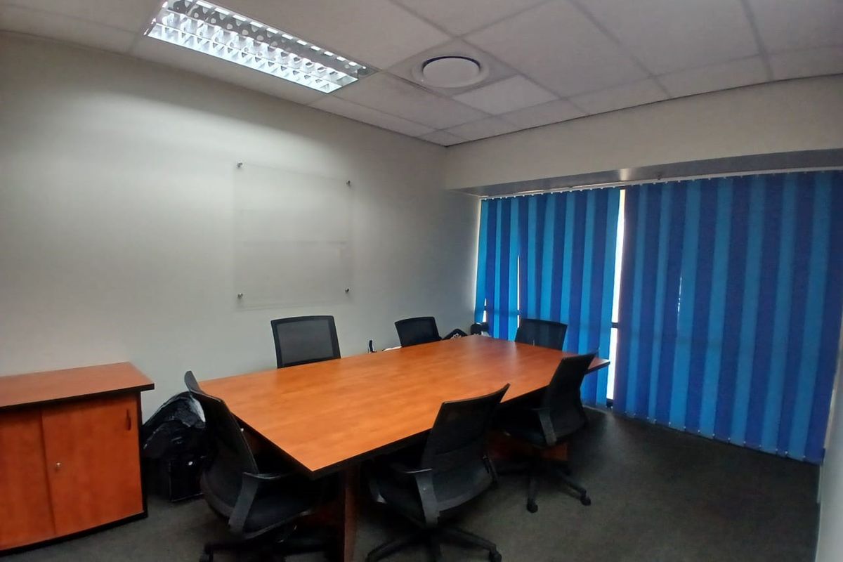 A functional office meeting room featuring a suspended ceiling, recessed lighting, and vertical window blinds.
