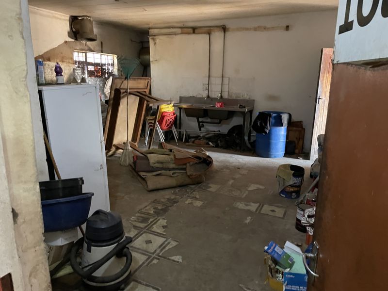 A utility or storage space featuring a stainless steel double sink, exposed plumbing, and damaged flooring, requiring significant renovation and repair.