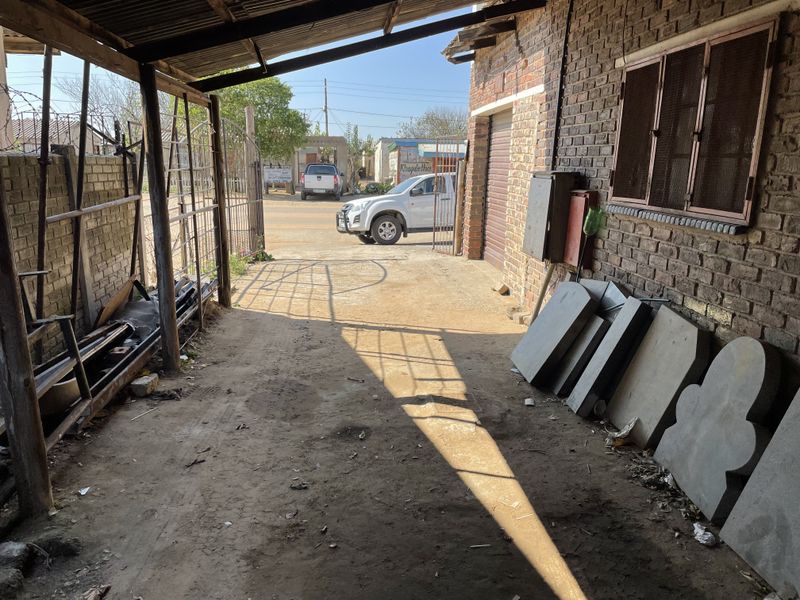 A covered outdoor utility or garage area featuring exposed brick walls, a corrugated iron roof, and a metal security gate leading to the street.