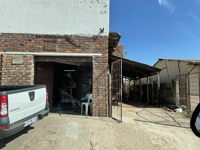 Front exterior view of a commercial property featuring a brick facade, metal security gate, and a covered side area with a concrete driveway.