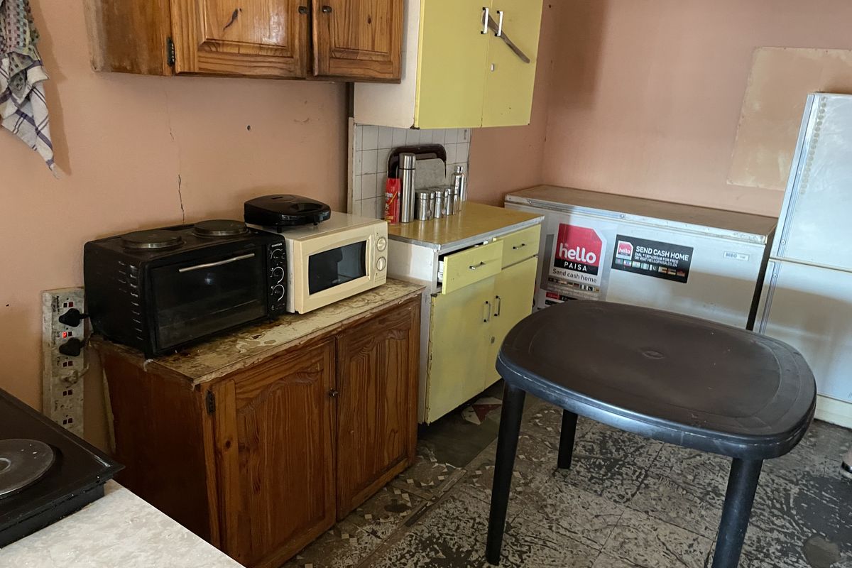 A dated kitchen area featuring original wooden cabinetry, tiled backsplash, and worn flooring, requiring significant renovation and modernization of fixed finishes.