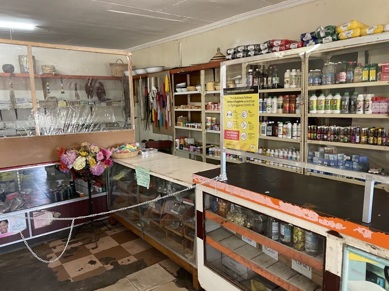 A retail service area featuring built-in shelving units, a service counter with a protective screen, and worn flooring, suitable for commercial use.