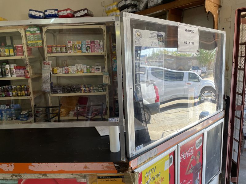 A service counter area featuring a protective glass partition and metal shelving units, typical of a retail or business utility space.