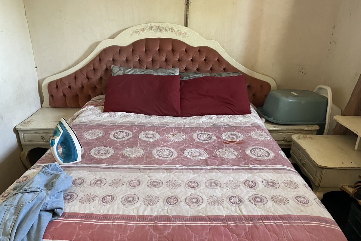 A bedroom featuring a built-in headboard, currently requiring significant wall repairs and cosmetic updates to improve the overall condition of the space.