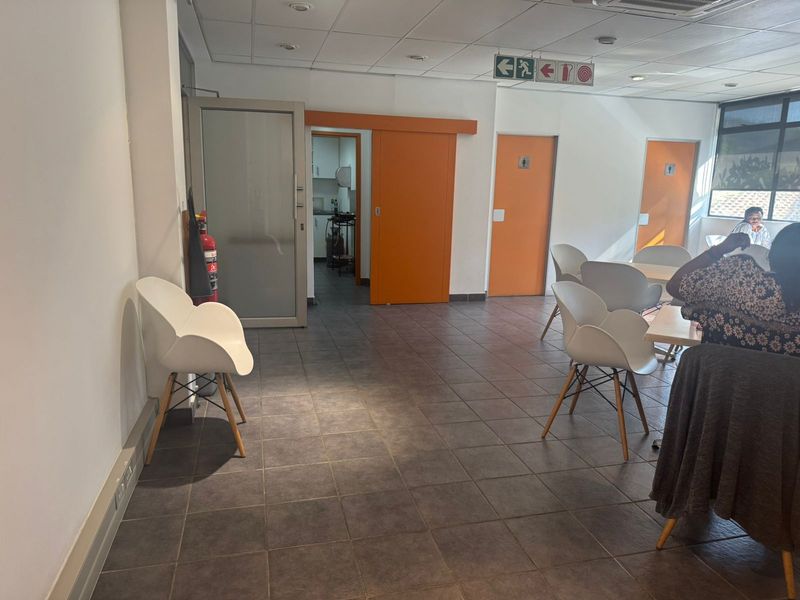 Open plan industrial office or communal area featuring tiled flooring, suspended ceilings, and access to secondary utility spaces.