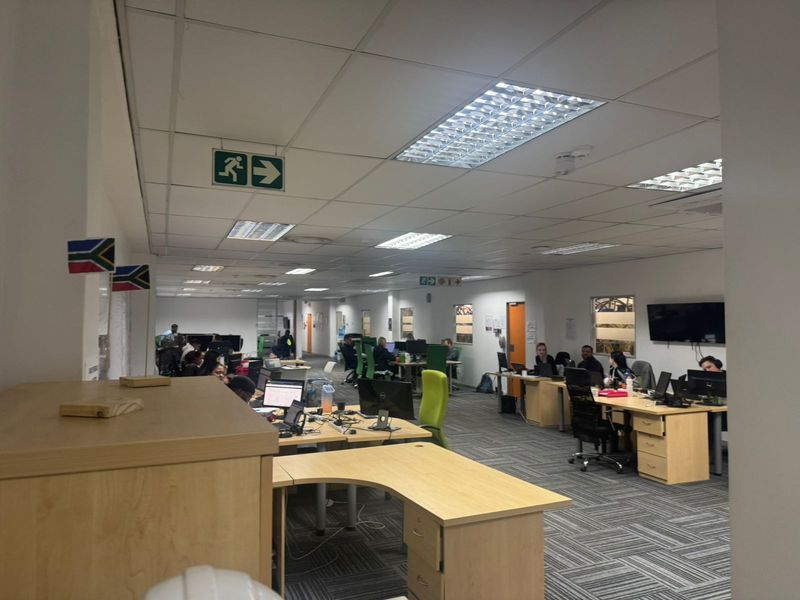 Open-plan industrial office space featuring suspended ceilings, recessed lighting, and carpeted flooring, currently configured for multiple workstations.