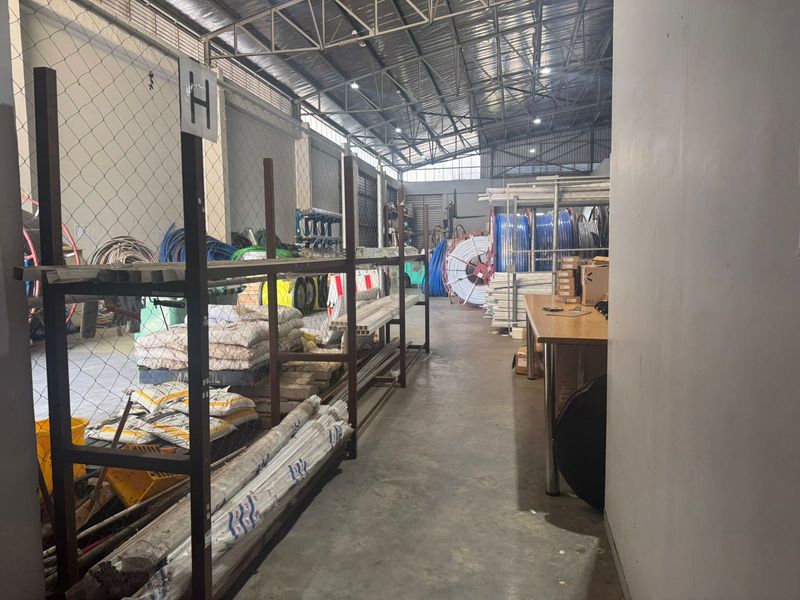 Industrial warehouse utility space featuring exposed steel roof trusses, concrete flooring, and partitioned storage areas.