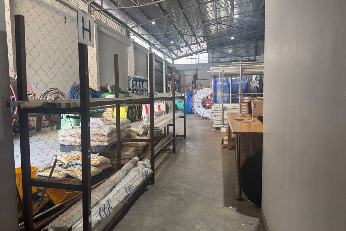 Industrial warehouse utility space featuring exposed steel roof trusses, concrete flooring, and partitioned storage areas.
