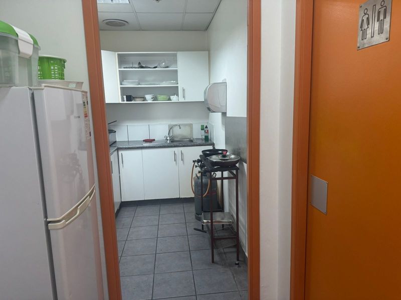 A functional industrial kitchenette featuring white cabinetry, a stainless steel sink, and tiled flooring, providing essential utility space for staff or office use.