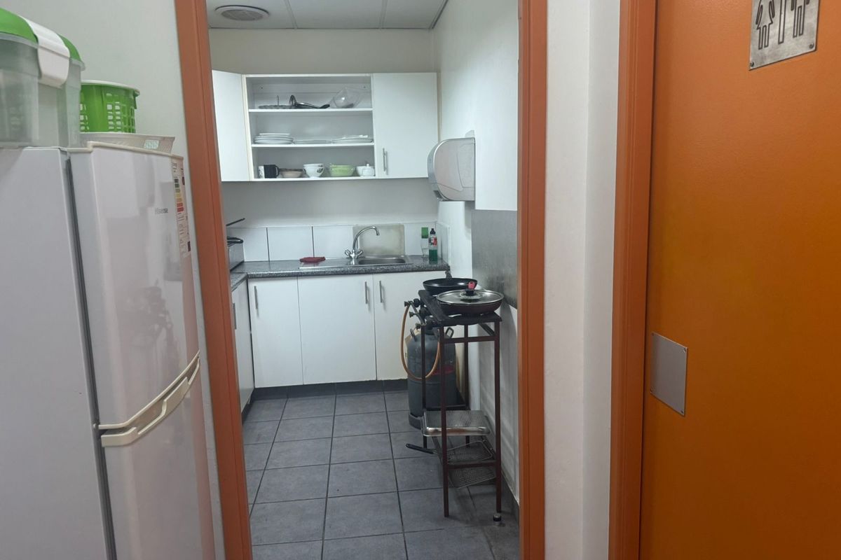 A functional industrial kitchenette featuring white cabinetry, a stainless steel sink, and tiled flooring, providing essential utility space for staff or office use.