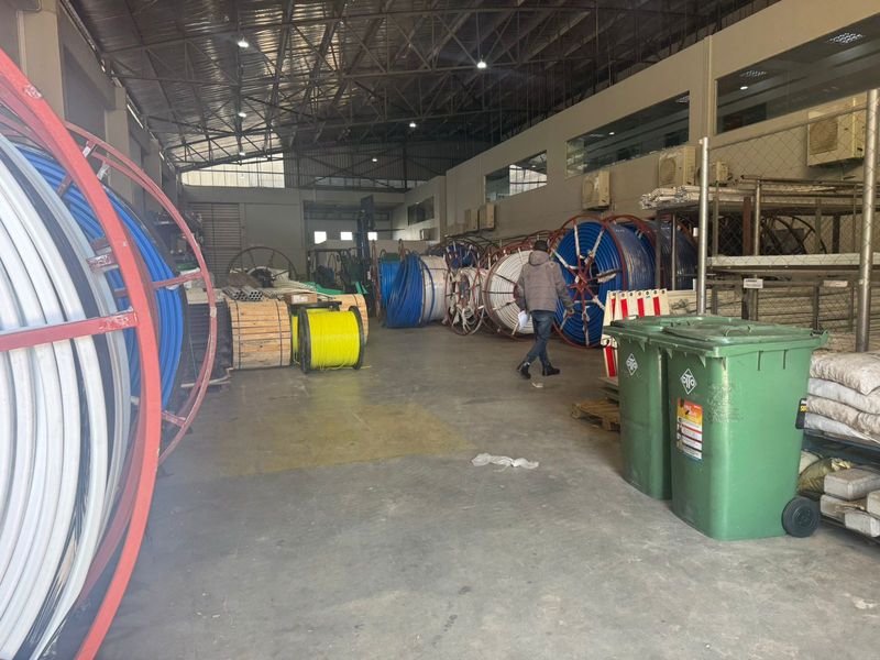 Spacious industrial warehouse featuring high ceilings with exposed steel trusses, concrete flooring, and mezzanine office access, suitable for storage or manufacturing operations.