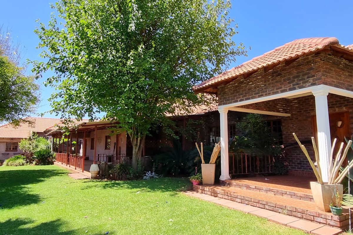 A view of the rear exterior of the guest house featuring a brick facade, tiled roof, and a spacious covered patio overlooking the garden.