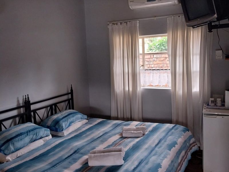 A cozy bedroom featuring a traditional thatched roof with exposed timber beams, tiled flooring, and a wall-mounted air conditioning unit.
