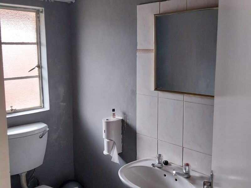 A compact bathroom featuring a standard toilet, pedestal washbasin, and tiled splashback, requiring cosmetic updates to the wall finishes and fixtures.