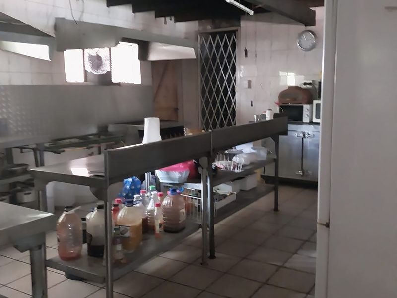 Commercial-style kitchen featuring stainless steel prep tables, tiled flooring, and exposed timber ceiling beams, suitable for high-volume food preparation.