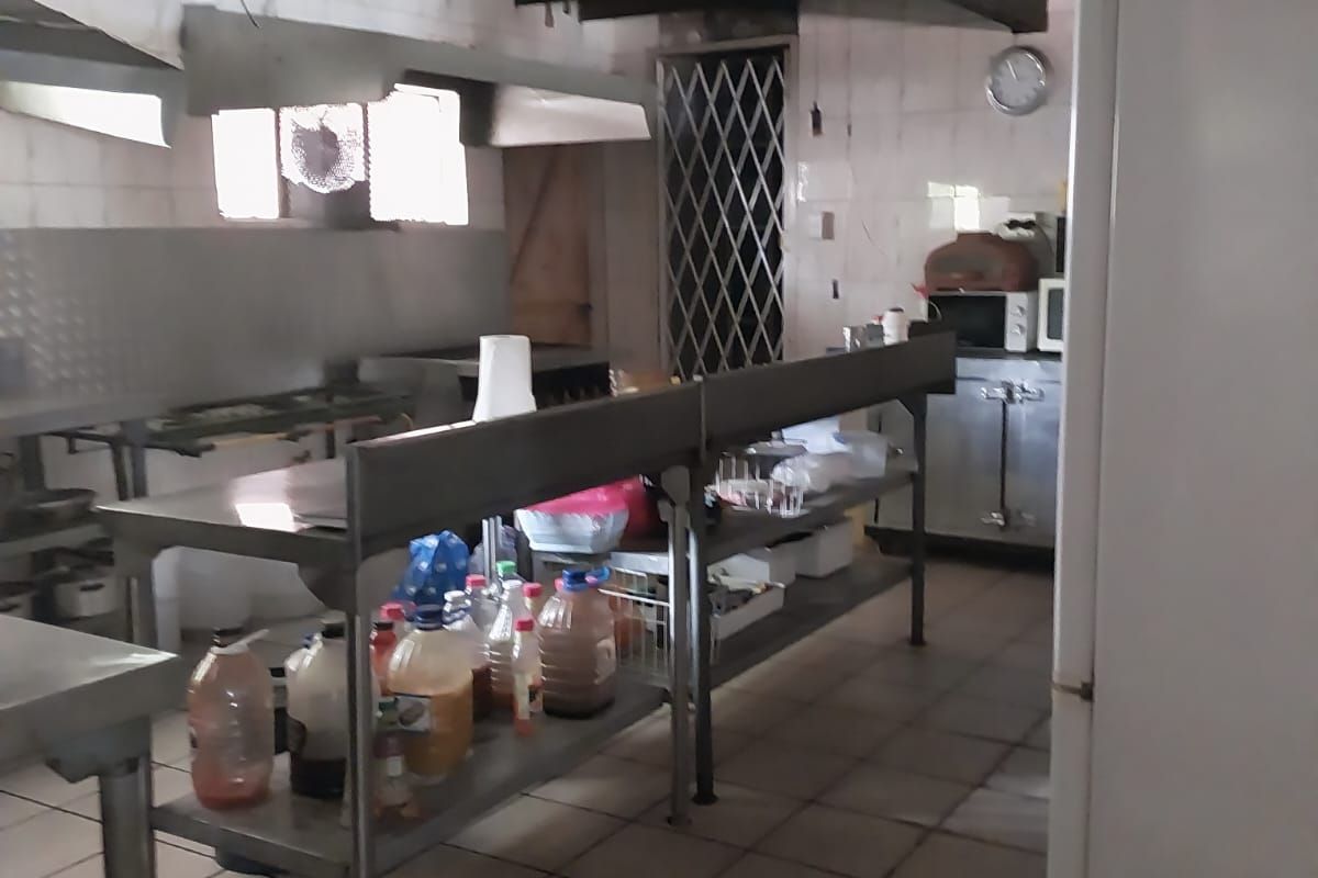 Commercial-style kitchen featuring stainless steel prep tables, tiled flooring, and exposed timber ceiling beams, suitable for high-volume food preparation.