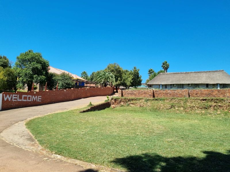 Front exterior view of the guest house property featuring a paved driveway, brick boundary walls, and a building with a traditional thatched roof.
