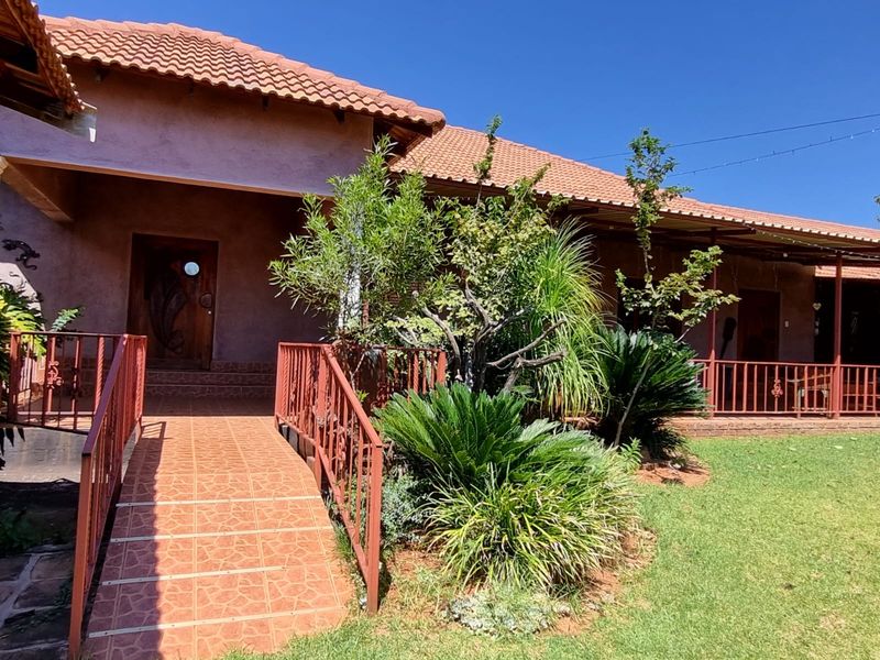 A well-maintained rear exterior view featuring a tiled access ramp, metal railings, and a covered patio area with terracotta roof tiles.