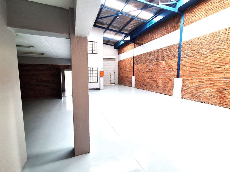 Spacious industrial warehouse unit featuring high ceilings with exposed steel trusses, durable epoxy flooring, and large brick walls, suitable for various commercial operations.