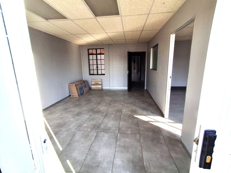 An empty, well-lit office space featuring neutral grey walls, large format floor tiles, and a suspended ceiling, suitable for various commercial or industrial uses.