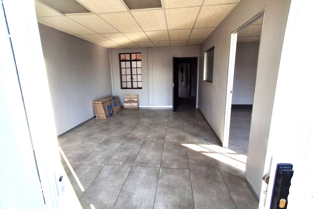 An empty, well-lit office space featuring neutral grey walls, large format floor tiles, and a suspended ceiling, suitable for various commercial or industrial uses.