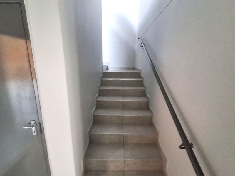 A functional industrial staircase featuring tiled steps, a sturdy metal handrail, and a metal door entrance.