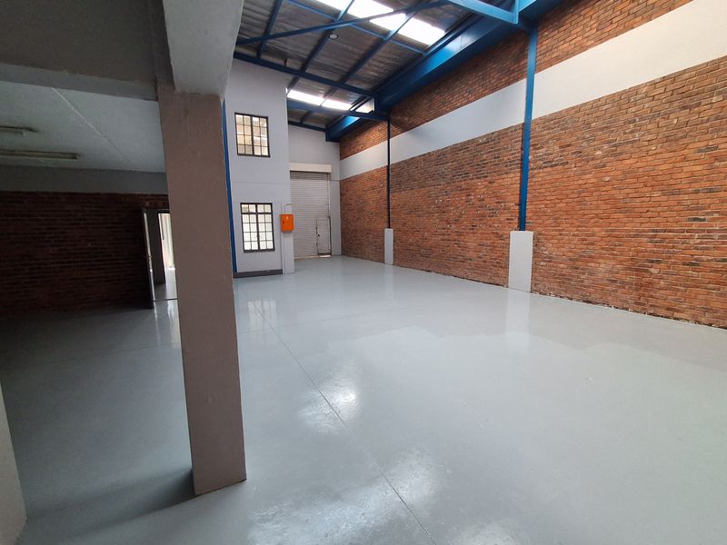 Spacious industrial warehouse unit featuring high ceilings with exposed steel trusses, durable epoxy-coated flooring, and large brick walls, suitable for various commercial or storage uses.