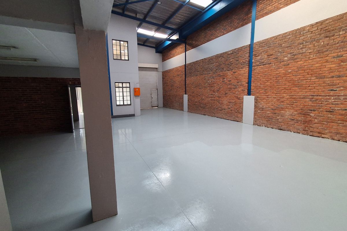 Spacious industrial warehouse unit featuring high ceilings with exposed steel trusses, durable epoxy-coated flooring, and large brick walls, suitable for various commercial or storage uses.