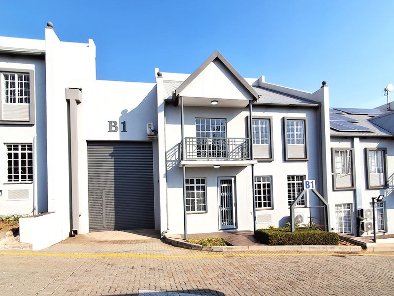 Front elevation of industrial unit B1 featuring a large roller shutter door, balcony, and paved driveway access.