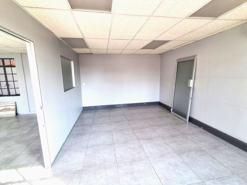 A clean, empty office space featuring neutral tiled flooring, a suspended ceiling, and a glass panel door, suitable for a professional workspace.