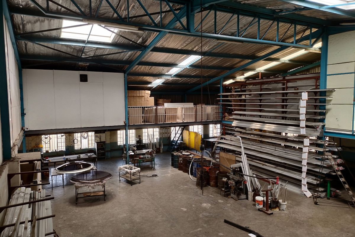 Spacious industrial warehouse featuring high-clearance ceilings, exposed steel trusses, mezzanine storage level, and concrete flooring suitable for manufacturing or storage operations.