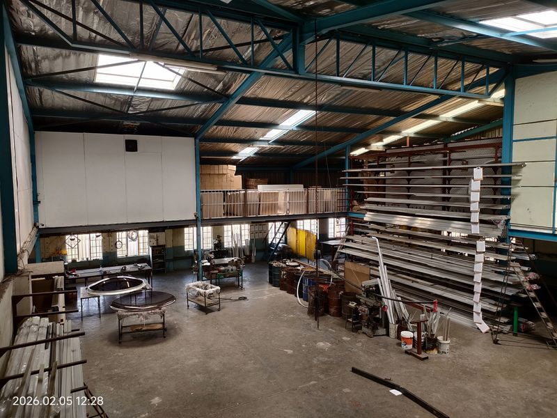 Spacious industrial warehouse featuring high-clearance ceilings, exposed steel trusses, mezzanine storage level, and concrete flooring suitable for manufacturing or storage operations.