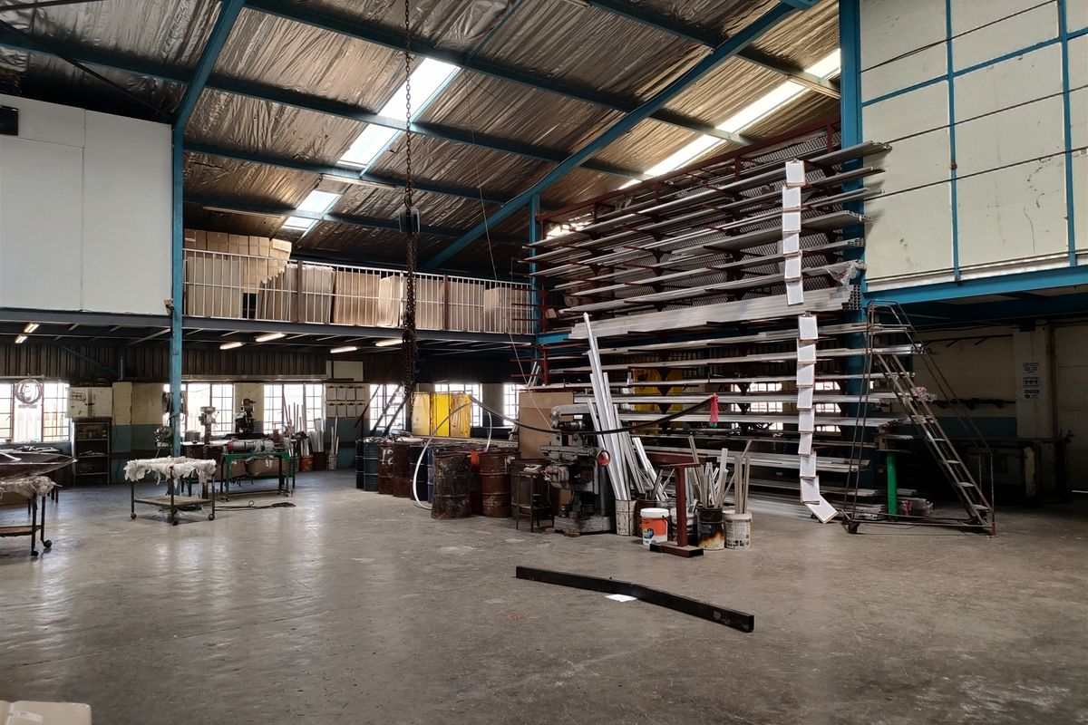 Spacious industrial warehouse featuring high ceilings with exposed steel trusses, a mezzanine level, concrete flooring, and integrated metal racking systems for storage.