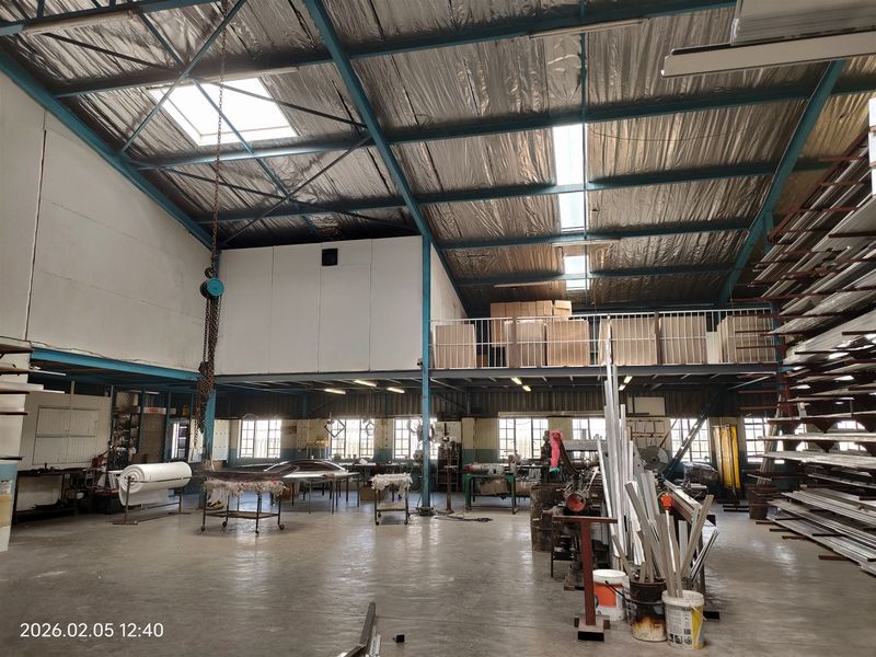 Spacious industrial warehouse featuring a high-clearance steel truss roof, mezzanine storage level, integrated skylights, and durable concrete flooring suitable for manufacturing or storage operations.