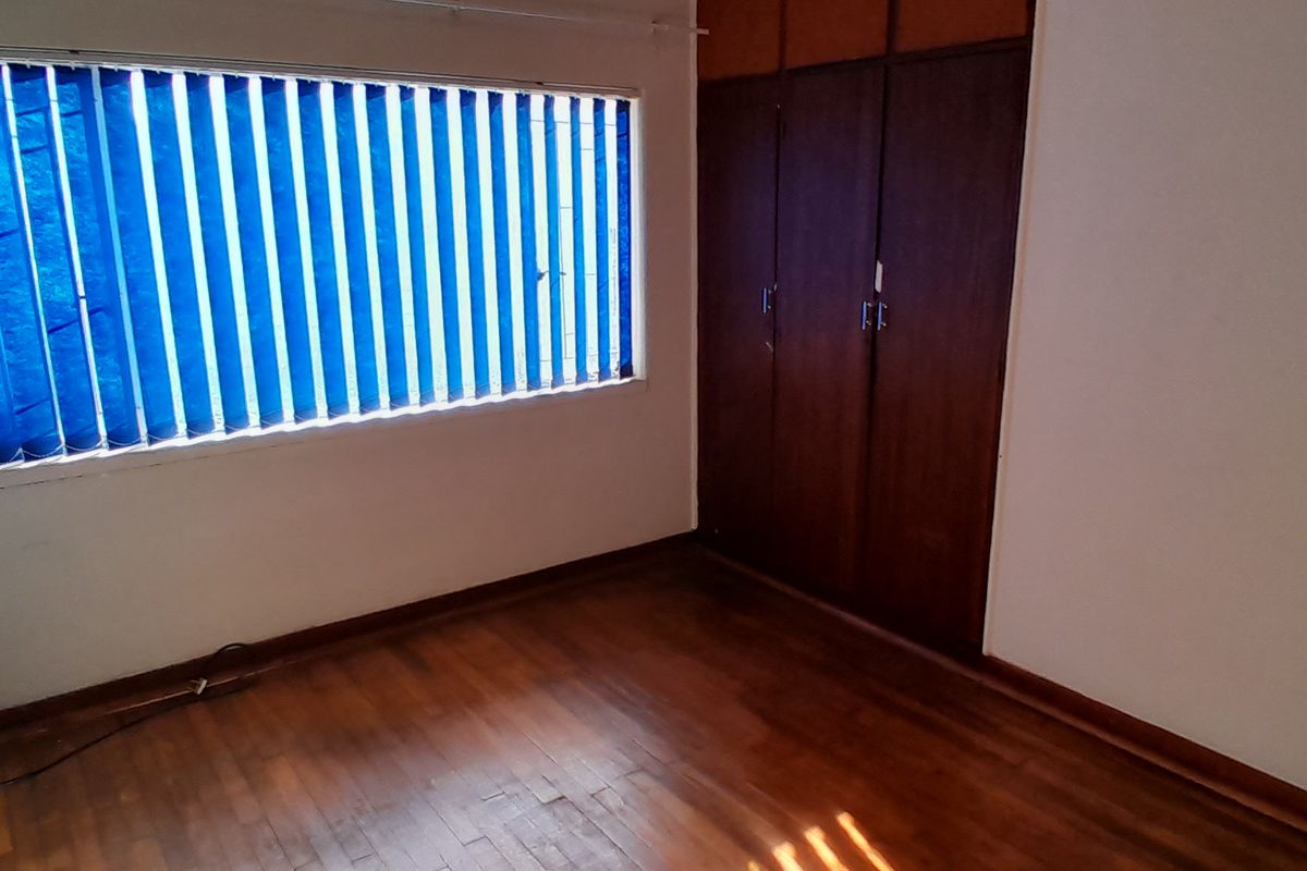 An empty bedroom featuring parquet flooring, built-in wooden cupboards, and vertical window blinds, offering a blank canvas for potential updates.