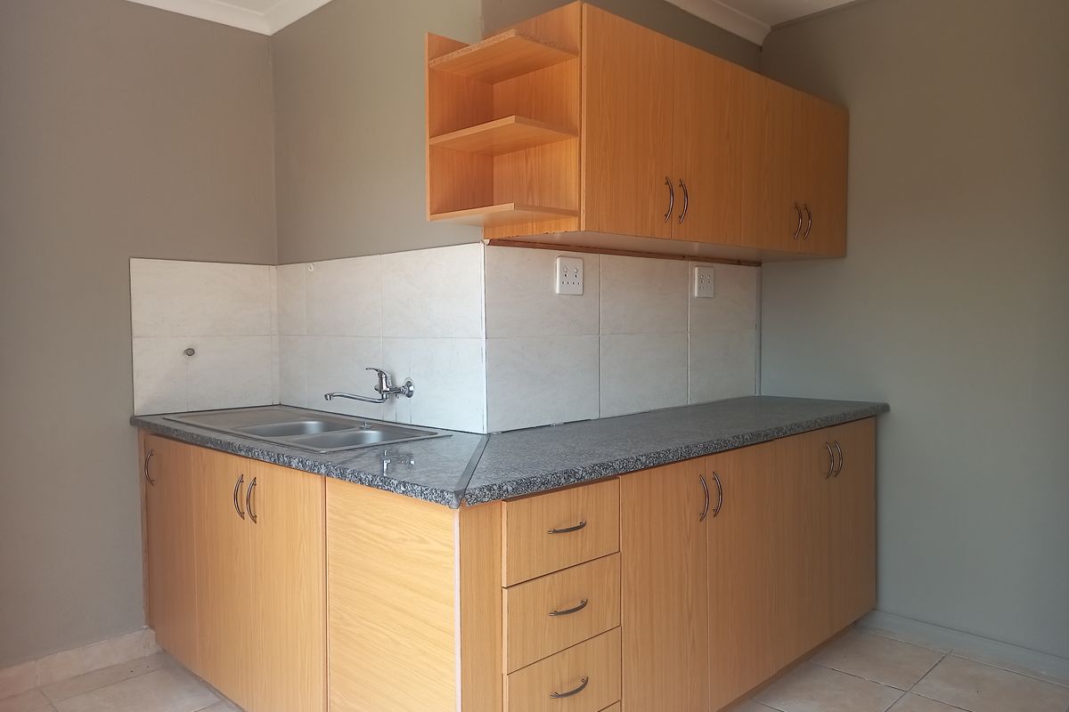 A compact kitchen area featuring light wood-look cabinetry, a granite-effect countertop, and a stainless steel double sink with tiled splashback.