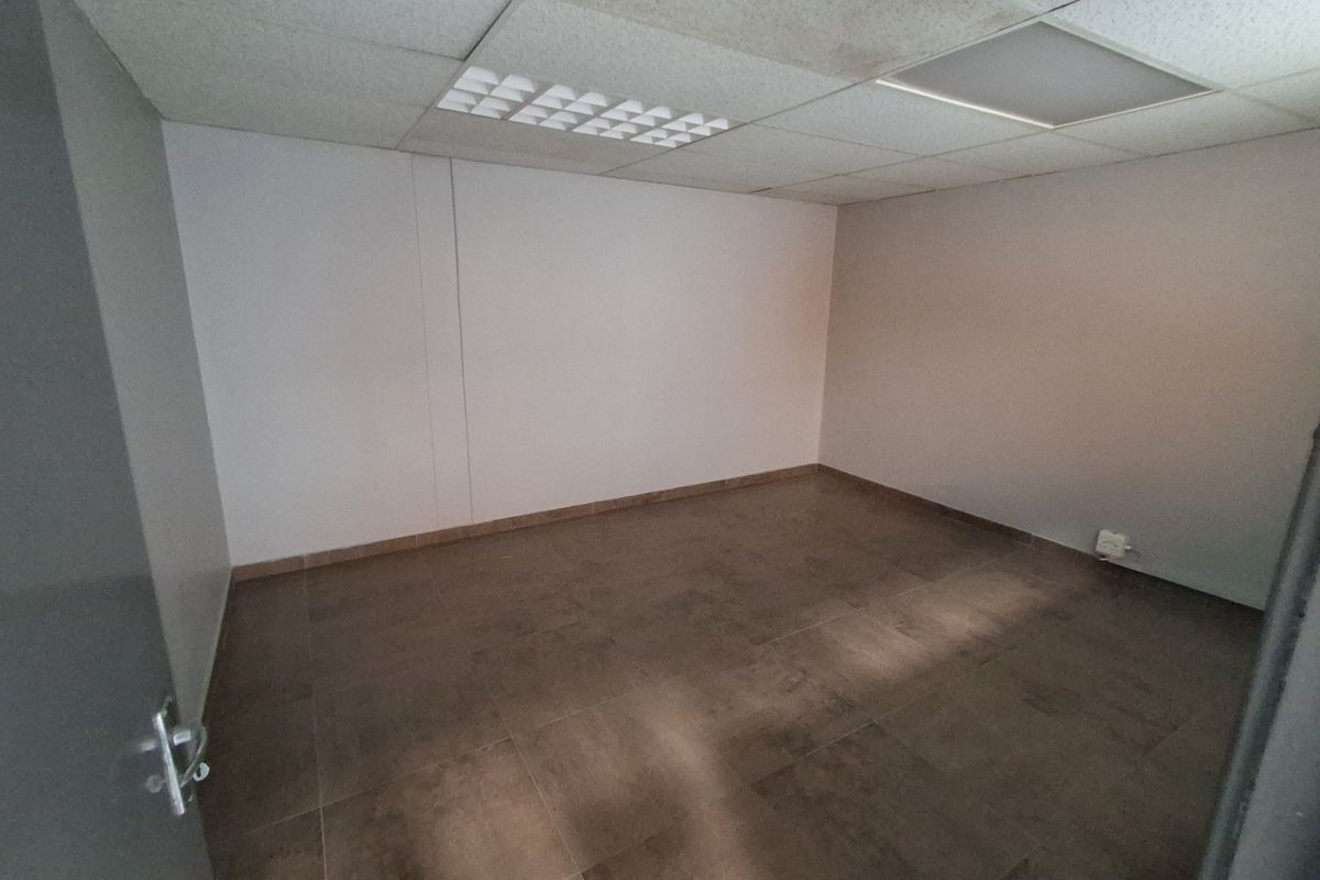 A clean, empty office space featuring tiled flooring, a suspended ceiling with integrated lighting, and neutral wall finishes.