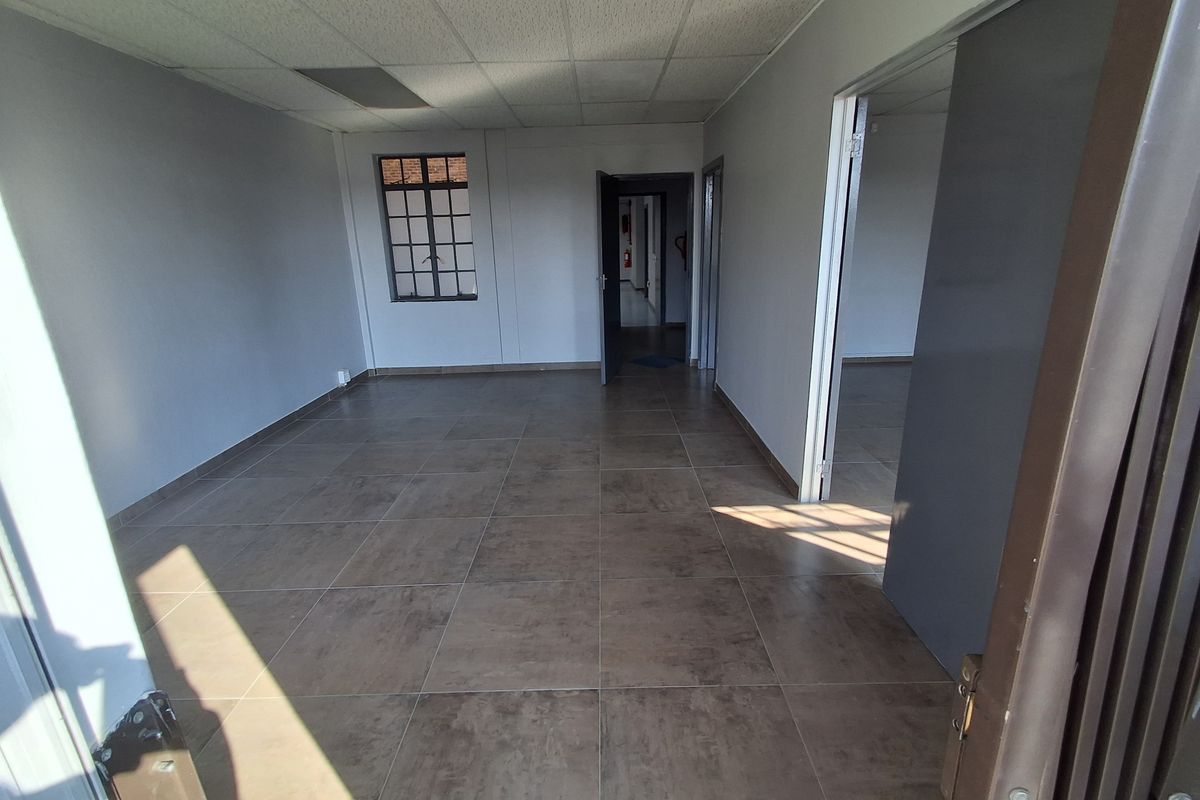 An empty industrial office space featuring large format floor tiles, a suspended acoustic ceiling, and multiple doorways leading to adjacent rooms.