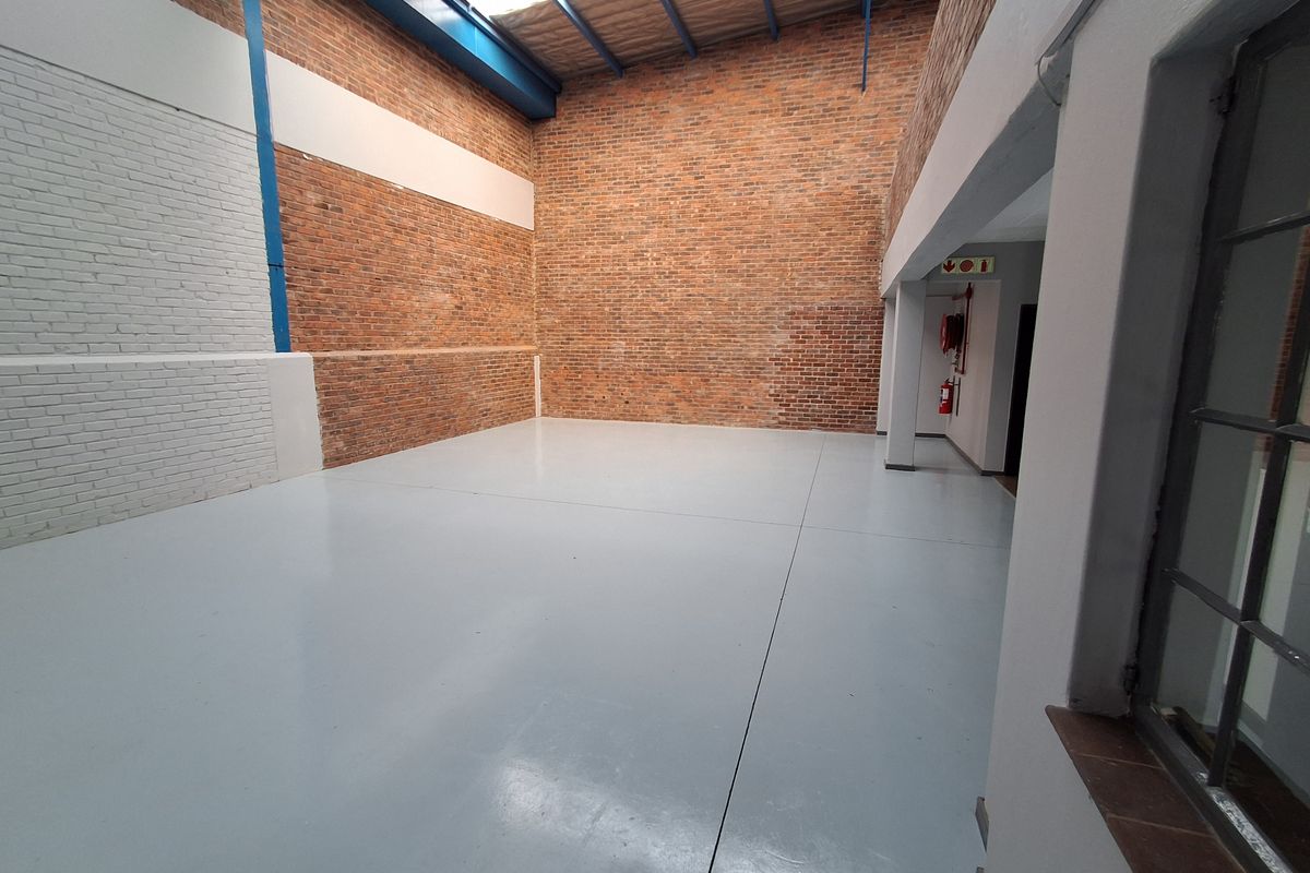 Spacious industrial warehouse unit featuring exposed brick walls, high ceilings with skylights, and polished concrete flooring.