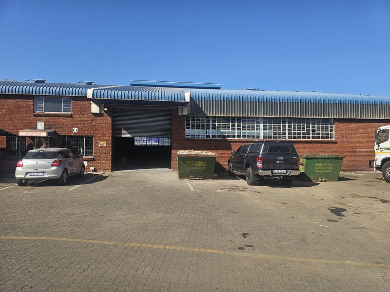 Front elevation of an industrial warehouse featuring a brick facade, large roller shutter door, and paved parking area.