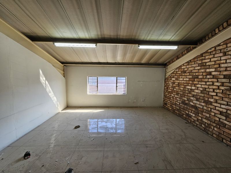 An empty industrial utility space featuring exposed brickwork, tiled flooring, and a corrugated metal ceiling with integrated fluorescent lighting.