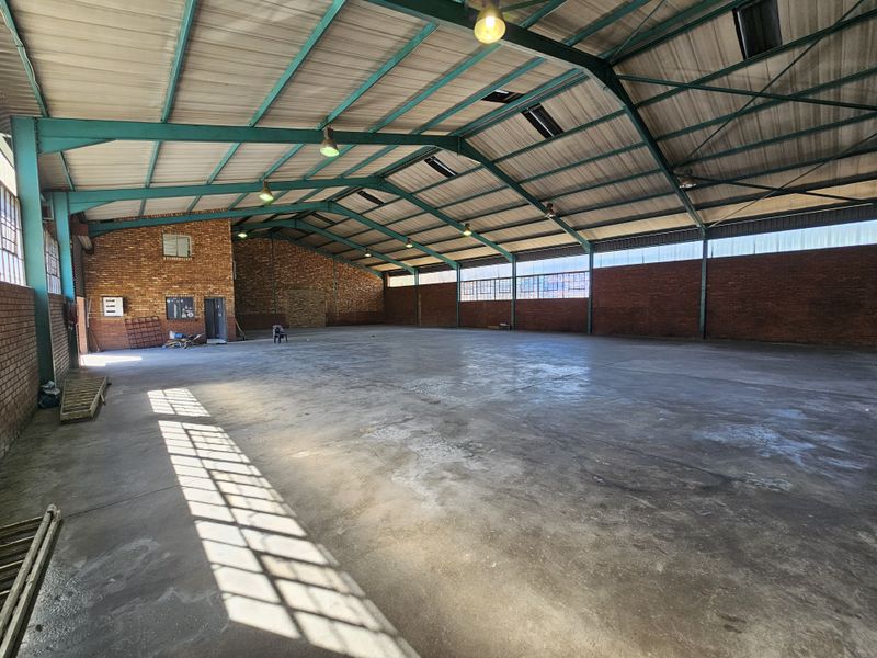 Spacious industrial warehouse featuring high exposed steel truss ceilings, durable concrete flooring, and expansive brick walls with natural light from clerestory windows.