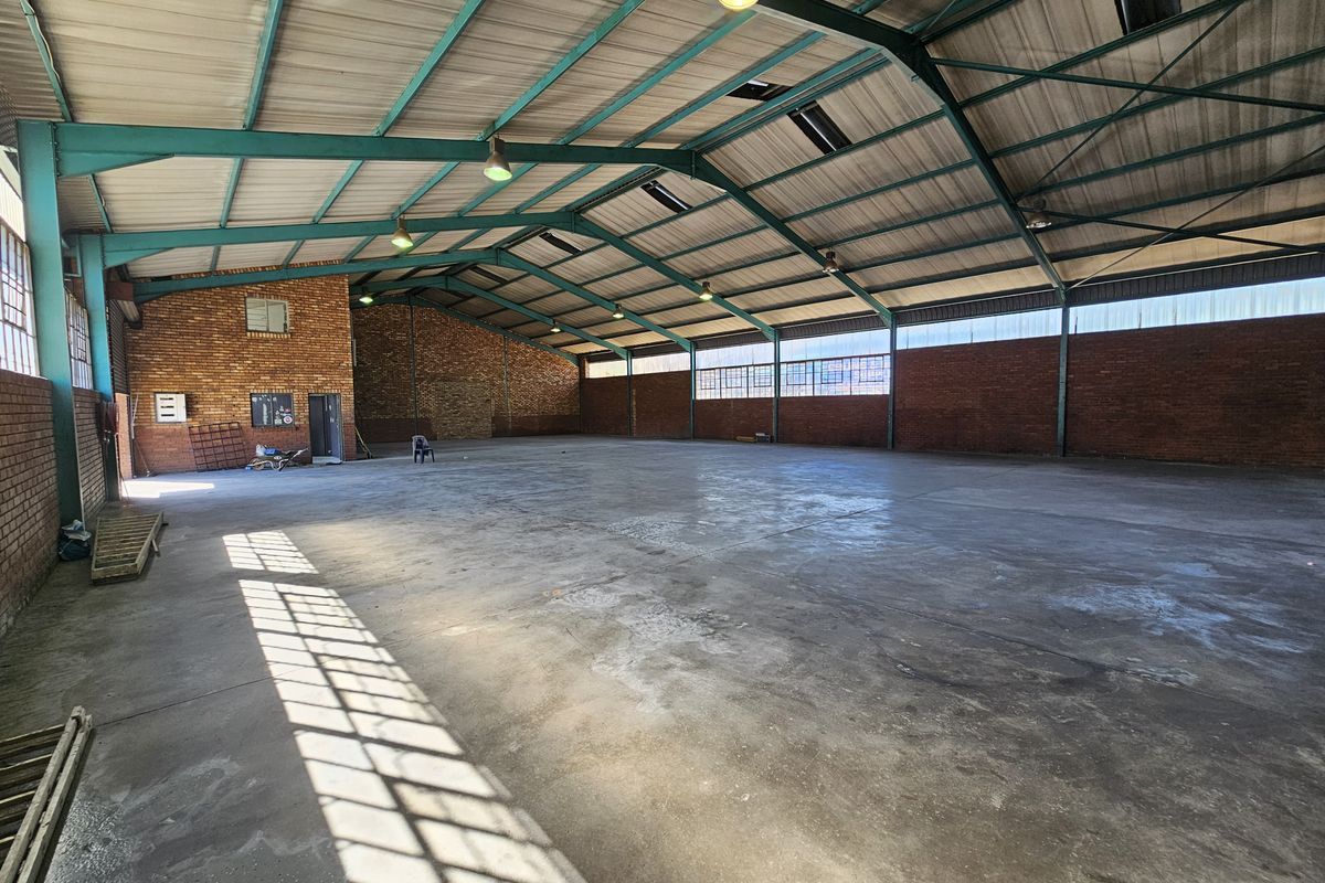 Spacious industrial warehouse featuring high exposed steel truss ceilings, durable concrete flooring, and expansive brick walls with natural light from clerestory windows.