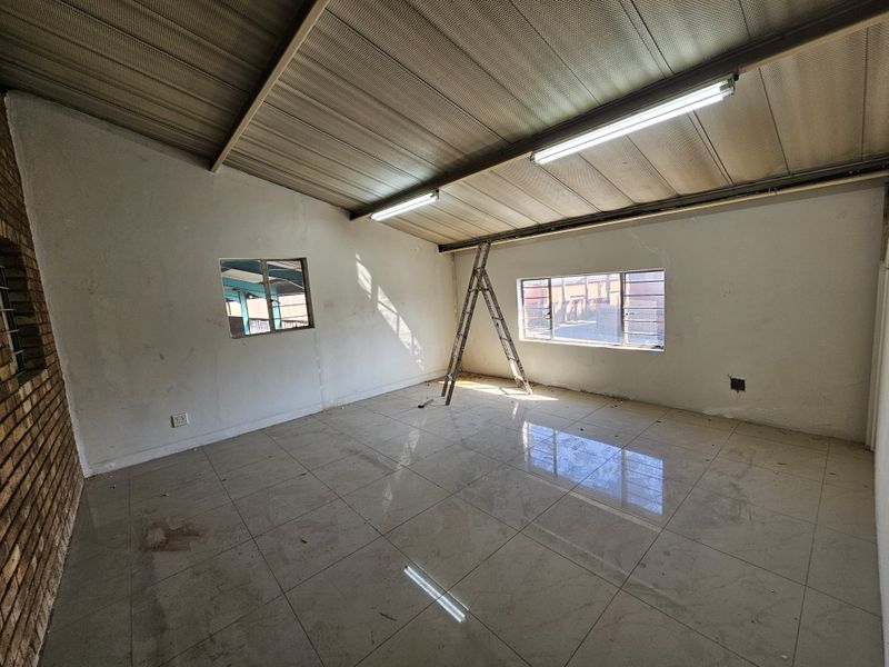 An empty industrial utility space featuring tiled flooring, exposed metal roofing, and natural light through steel-framed windows.