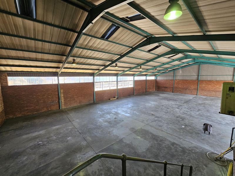 Spacious industrial warehouse unit featuring high exposed steel truss ceilings, concrete flooring, brick walls, and natural light from integrated skylights.