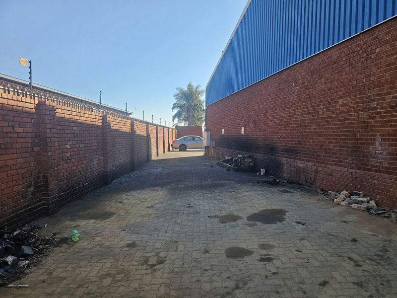 Rear exterior service area featuring brick boundary walls with electric fencing, paved ground surface, and industrial corrugated metal wall cladding.
